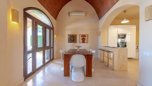 A dining area with a wooden table and chairs, an arched ceiling, and a kitchen in the background. - VESTA - Superior Villa - 3BR - North Golf I (Hurghada)