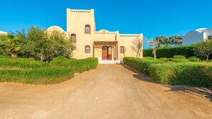 A building with a central entrance, surrounded by well-maintained hedges and a clear sky. - VESTA - Superior Villa - 3BR - North Golf I (Hurghada)