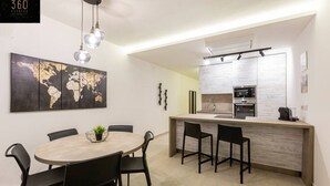 A modern kitchen with a central island, a dining area with a round table and chairs, and a world map artwork on the wall. - Beautiful, cozy APT just off the Promenade & WIFI (Tas-Sliema)