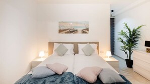 A modern bedroom with a large bed, two bedside tables with lamps, a potted plant, and a beach-themed artwork on the wall. - Beautiful, cozy APT just off the Promenade & WIFI (Tas-Sliema)