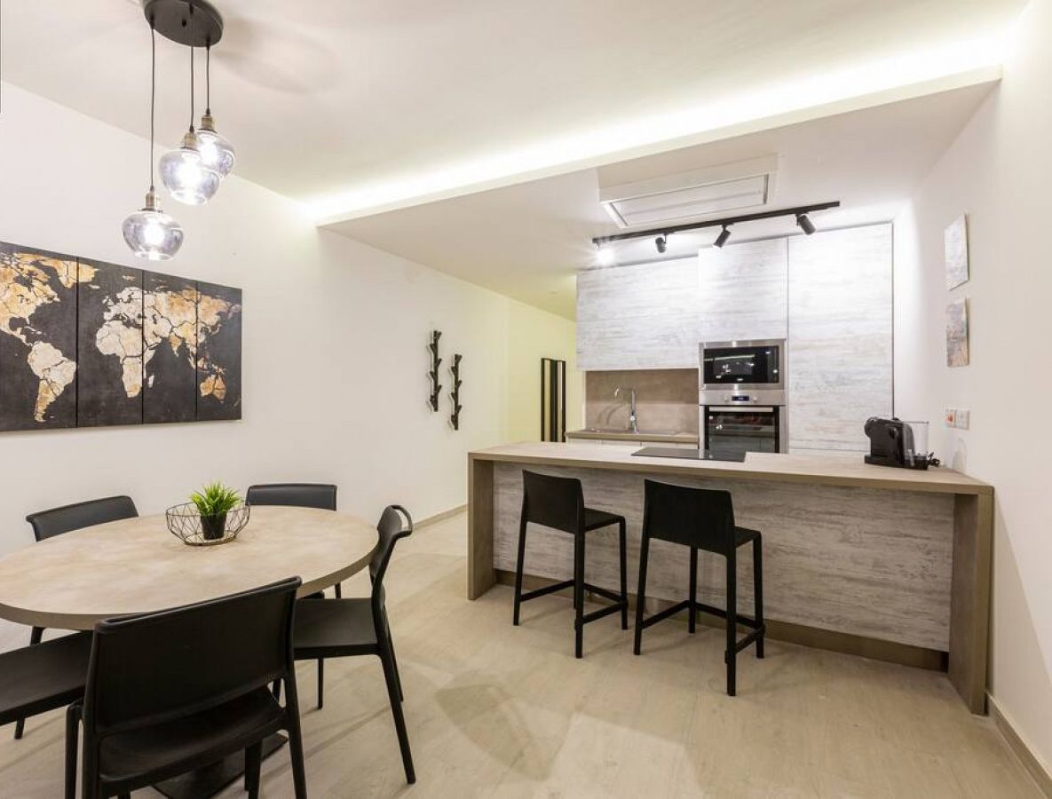 A modern kitchen with a central island, a dining area with a round table and chairs, and a world map artwork on the wall.