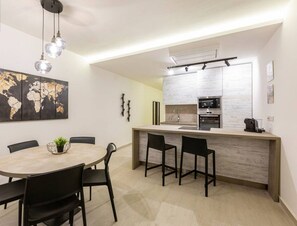 A modern kitchen with a central island, a dining area with a round table and chairs, and a world map artwork on the wall. - Beautiful, cozy APT just off the Promenade & WIFI (Tas-Sliema)