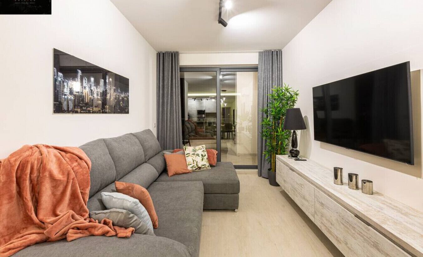 Un salon moderne avec un canapé gris, un téléviseur à écran plat et une console au design minimaliste.