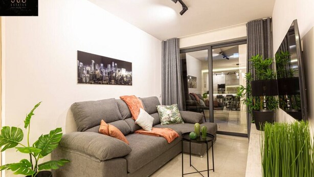 Ein modernes Wohnzimmer mit grauem Sofa, einem Stadtbildgemälde und Blick in den Küchenbereich.