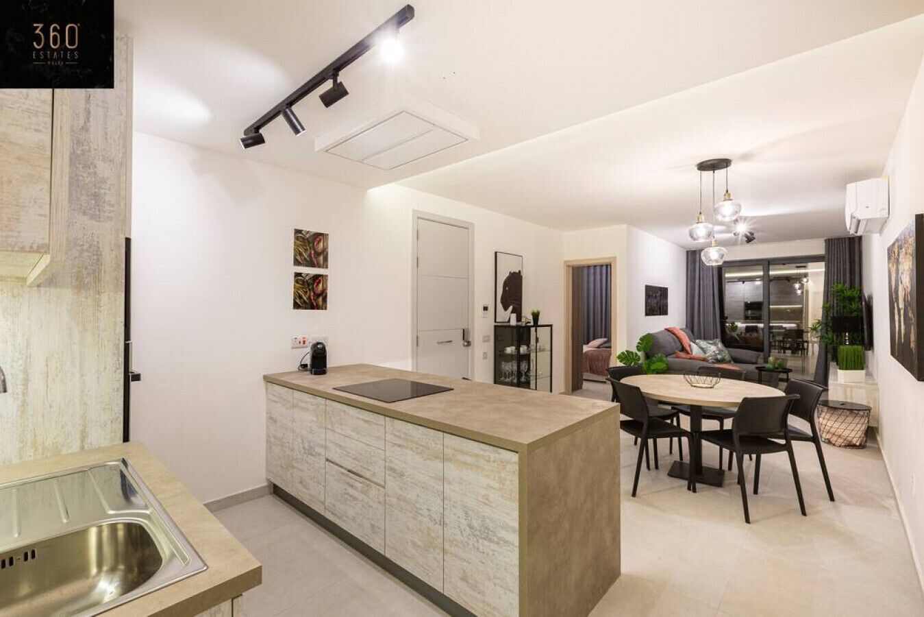 A modern kitchen with a central island, a dining area with a round table and chairs, and a living space with a sofa and a coffee table.