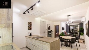 Eine moderne Küche mit Kochinsel, ein Essbereich mit rundem Tisch und Stühlen sowie ein Wohnbereich mit Sofa und Couchtisch.