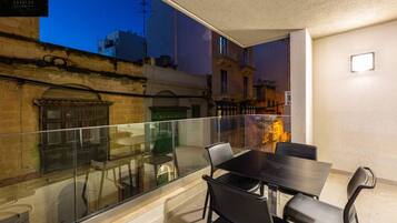 A modern balcony with a glass railing, a dining table, and chairs.