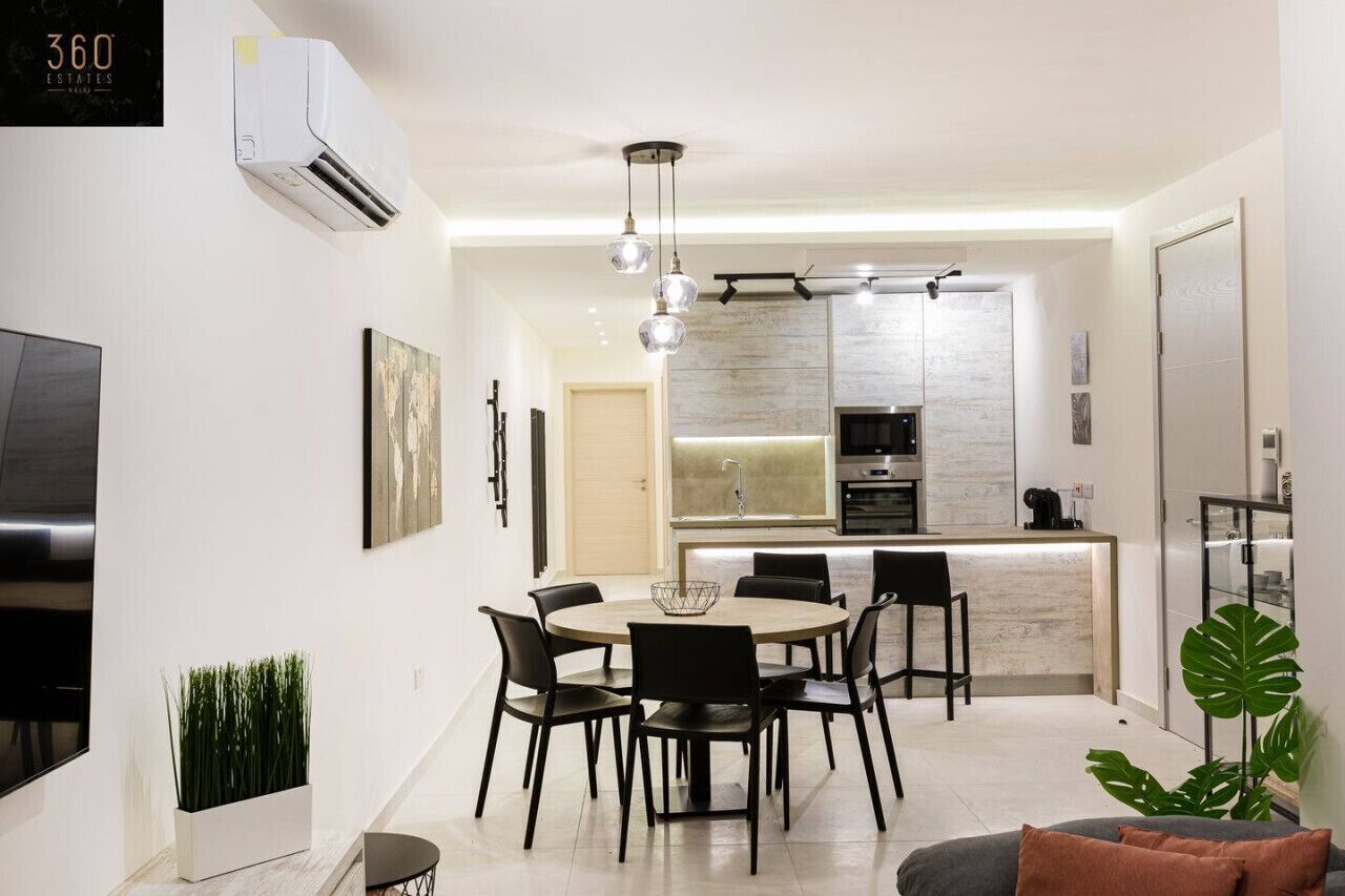 Une cuisine moderne dotée d’un îlot central, un coin repas avec une table ronde et des chaises, et un espace de détente avec un canapé et une plante.