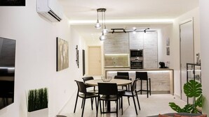 Une cuisine moderne dotée d’un îlot central, un coin repas avec une table ronde et des chaises, et un espace de détente avec un canapé et une plante.