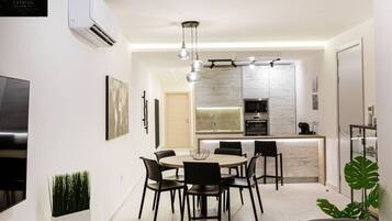 Une cuisine moderne dotée d’un îlot central, un coin repas avec une table ronde et des chaises, et un espace de détente avec un canapé et une plante.