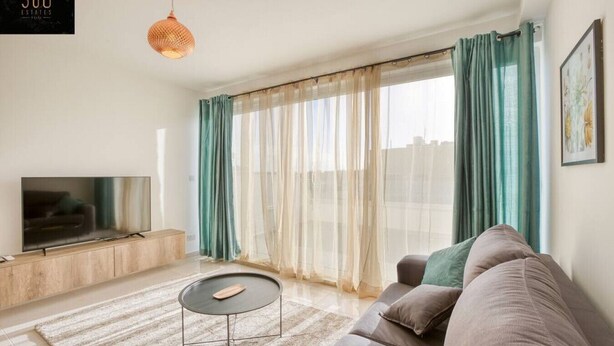 A modern living room with a flat-screen TV, a round coffee table, a sofa, and a large window with sheer curtains. - A beautiful, spacious penthouse (Il-Gżira)