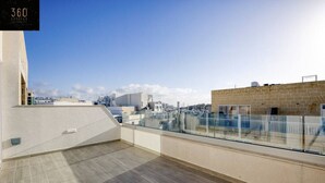 A rooftop terrace with a glass balustrade, a tiled floor, and a clear view of the cityscape. - A beautiful, spacious penthouse (Il-Gżira)