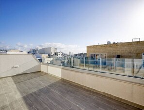 A rooftop terrace with a glass balustrade, a tiled floor, and a clear view of the cityscape.