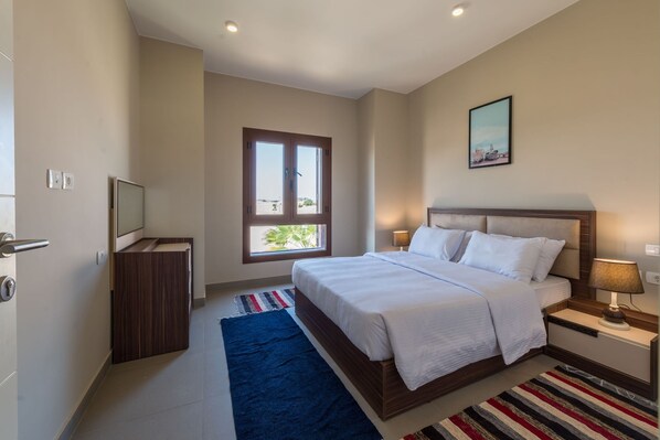 A bedroom with a bed, bedside tables, a TV, a window, and a painting on the wall.