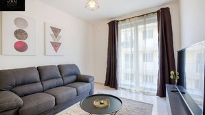 A modern living room with a grey sofa, a round coffee table, and a large window with curtains. - Brand new central APT with strong WIFI & Comfy Bed (Il-Gżira)