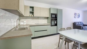 A modern kitchen with a marble countertop, built-in appliances, and a dining area with a glass table and chairs. - Brand new central APT with strong WIFI & Comfy Bed (Il-Gżira)