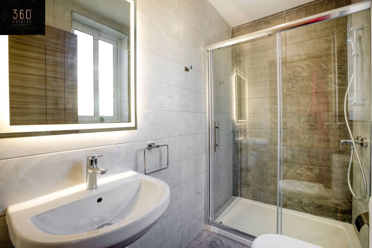 Een moderne badkamer met een witte wastafel, een douchecabine van glas en een grote spiegel.