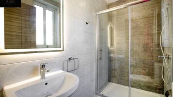 Een moderne badkamer met een witte wastafel, een douchecabine van glas en een grote spiegel.