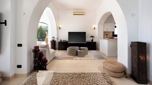 A modern living room with a flat-screen TV, a sofa, and a coffee table. There is a kitchen area in the background.