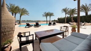 A poolside area with lounge chairs, a wooden table, and a wicker chair.