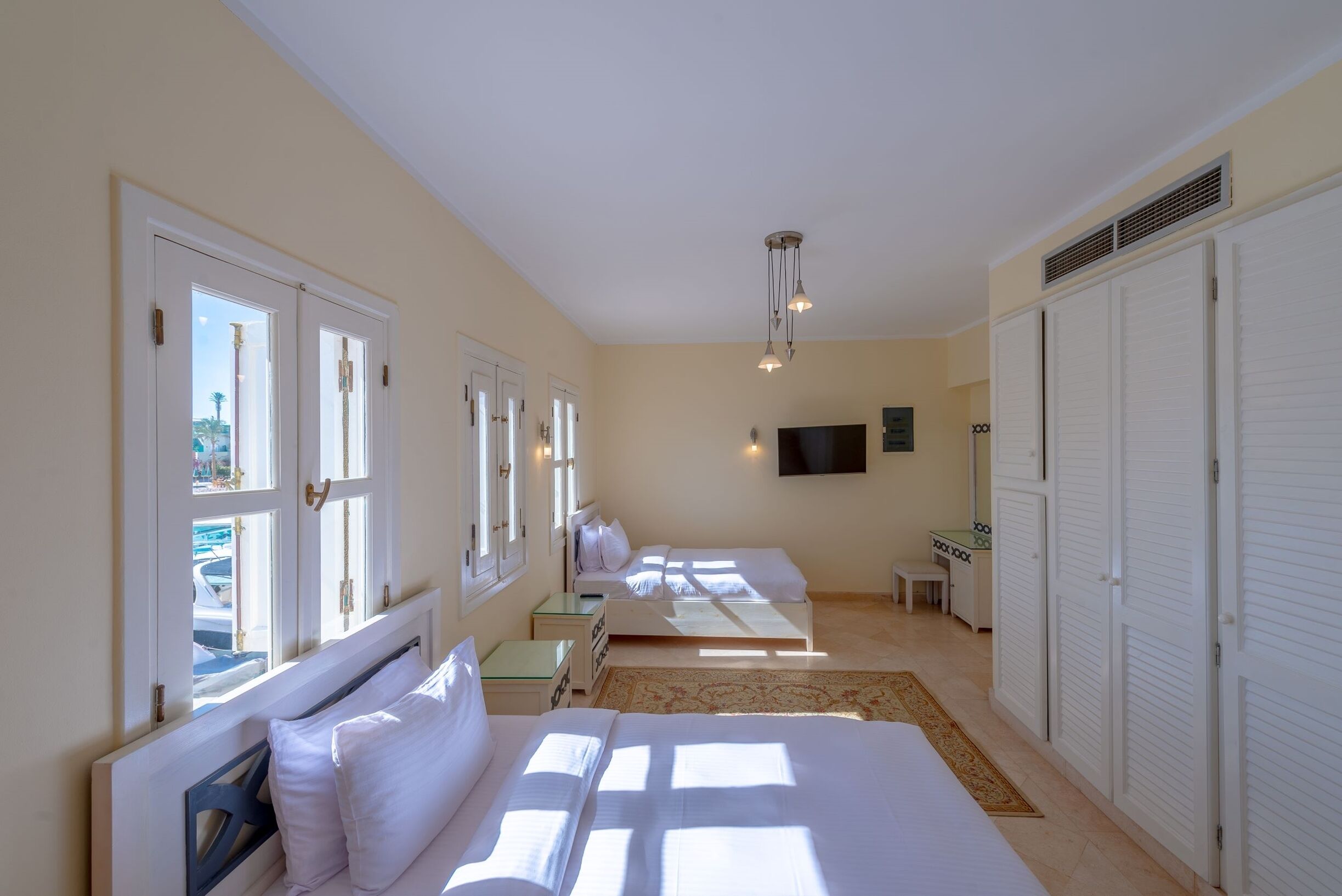 A hotel room with two beds, a TV mounted on the wall, and a window with a view of the outside.