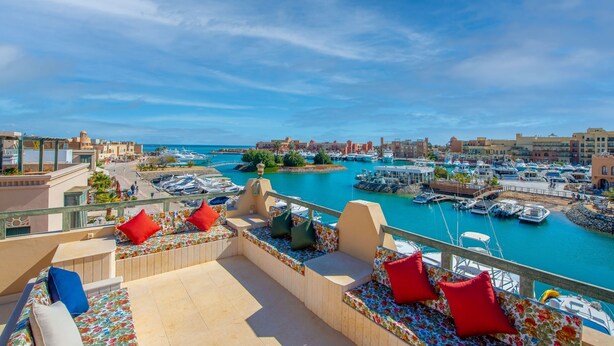 Une terrasse avec des sièges et une vue sur un port de plaisance où sont amarrés des bateaux.