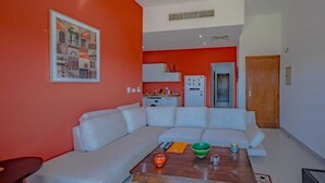 Ein modernes Wohnzimmer mit einem weißen Ecksofa, einem Holztisch und einer Küchenzeile im Hintergrund.