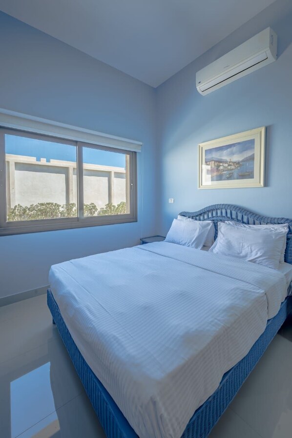A bedroom with a large bed, a window, and an air conditioning unit.