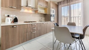 Eine moderne Küche mit Holzschränken, einem Gasherd, einem Wasserkocher und einem Essbereich mit Tisch und Stühlen.