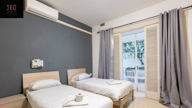 A hotel room with two beds, a window with curtains, an air conditioning unit, and a wall-mounted control panel. - Spacious NUM1 house in Swieqi - Sleeps 18 w/WIFI (Is-Swieqi)