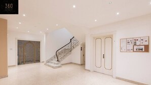 A spacious hallway with a marble staircase, a bulletin board with notices, and a door with a decorative frame. - Spacious NUM1 house in Swieqi - Sleeps 18 w/WIFI (Is-Swieqi)