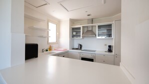 Eine moderne Küche mit weißen Arbeitsplatten, einem eingebauten Ofen und einem Fenster, das für natürliches Licht sorgt.