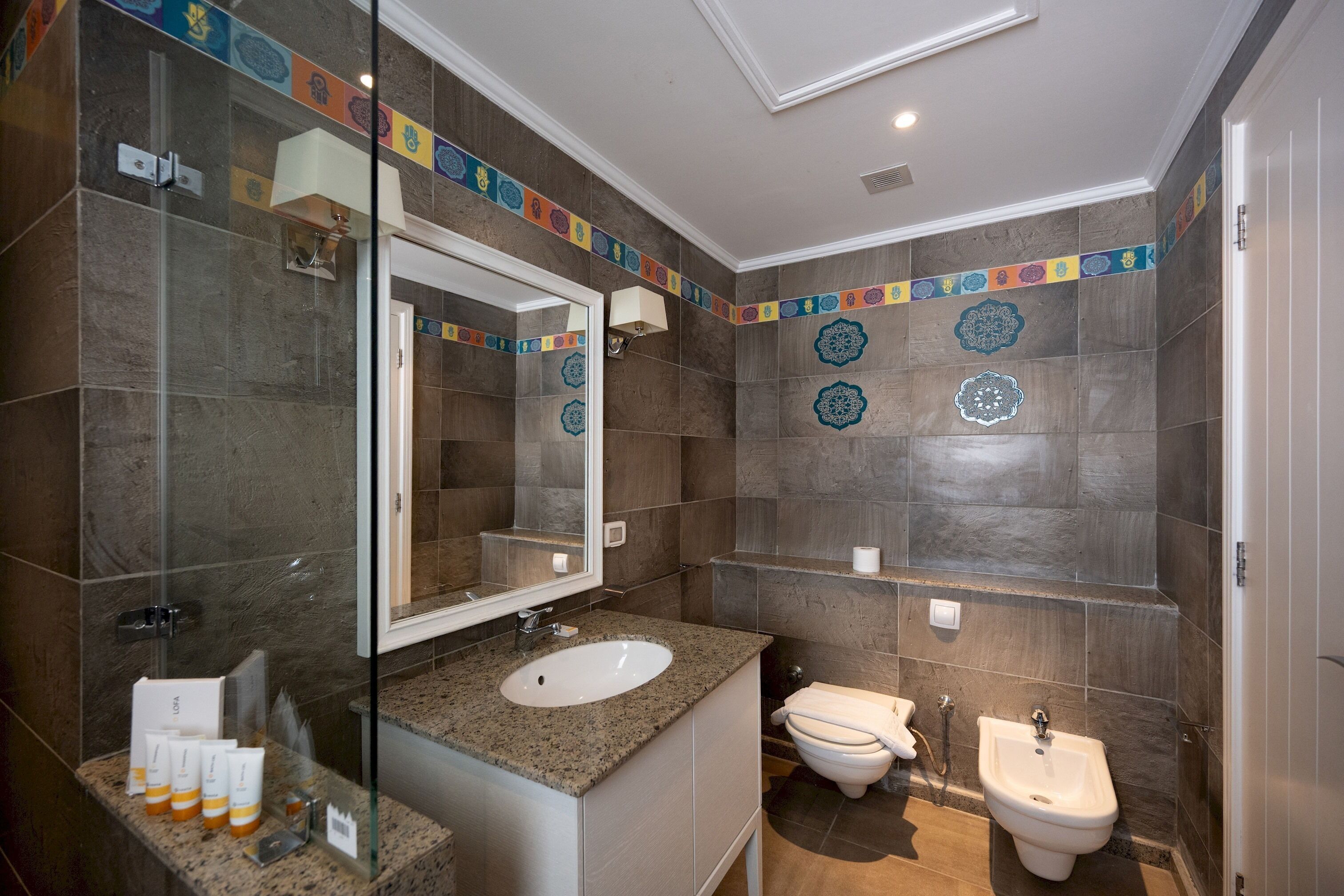 A modern bathroom with a granite countertop sink, a large mirror, a toilet, and a bidet.