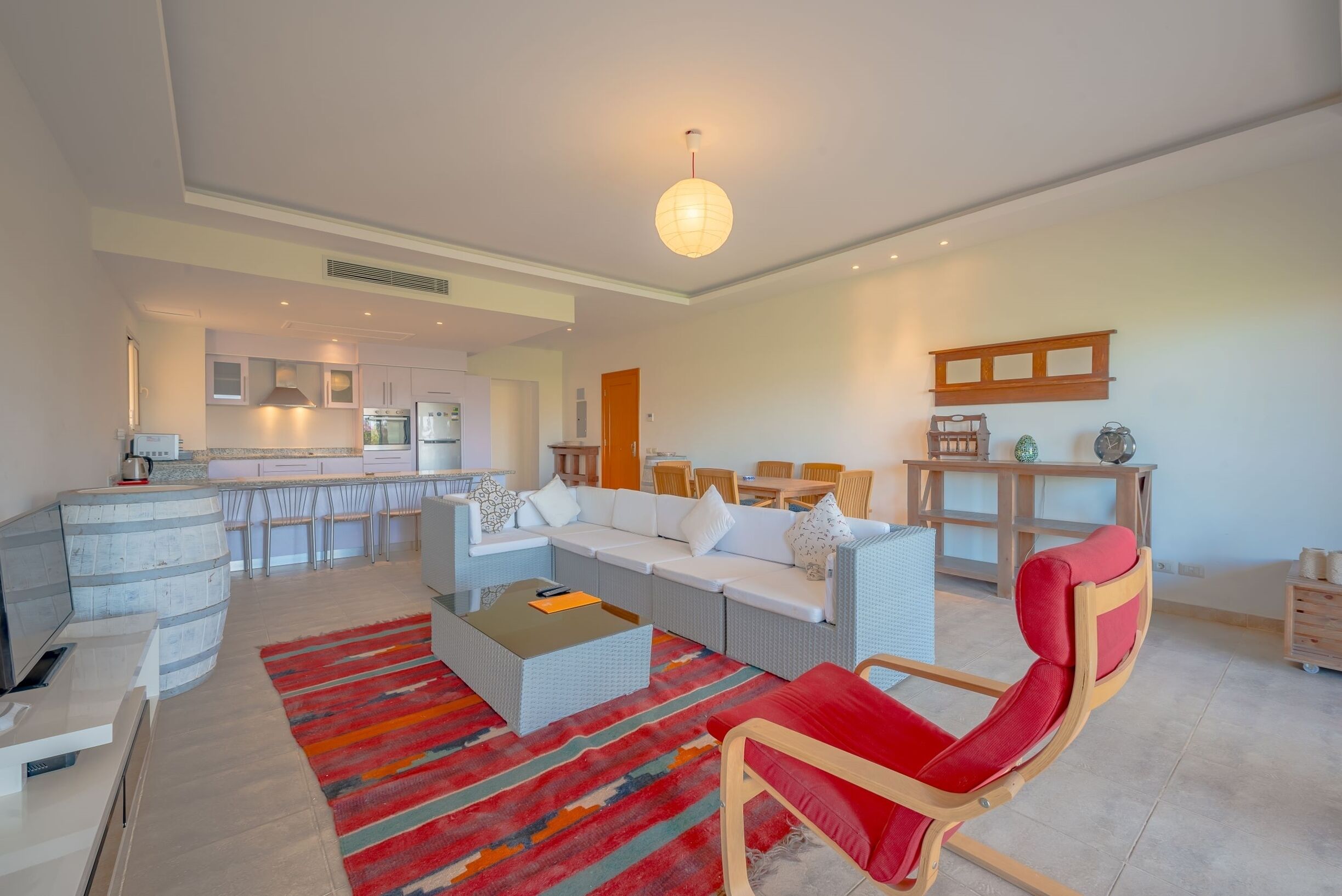 A modern living room with a sofa, a red chair, a coffee table, and a kitchen area in the background.