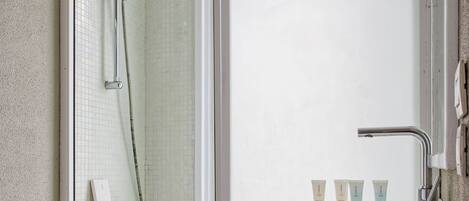 A bathroom with a glass shower enclosure, a sink with three toiletries, and a tiled backsplash.