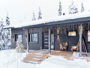 A wooden cabin with a porch, snow-covered trees, and a small Christmas tree. - Villa huili by Interhome (Kuusamo)