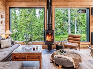 L’intérieur chaleureux d’un chalet avec un poêle à bois, de grandes fenêtres, un fauteuil en cuir et une table rustique.