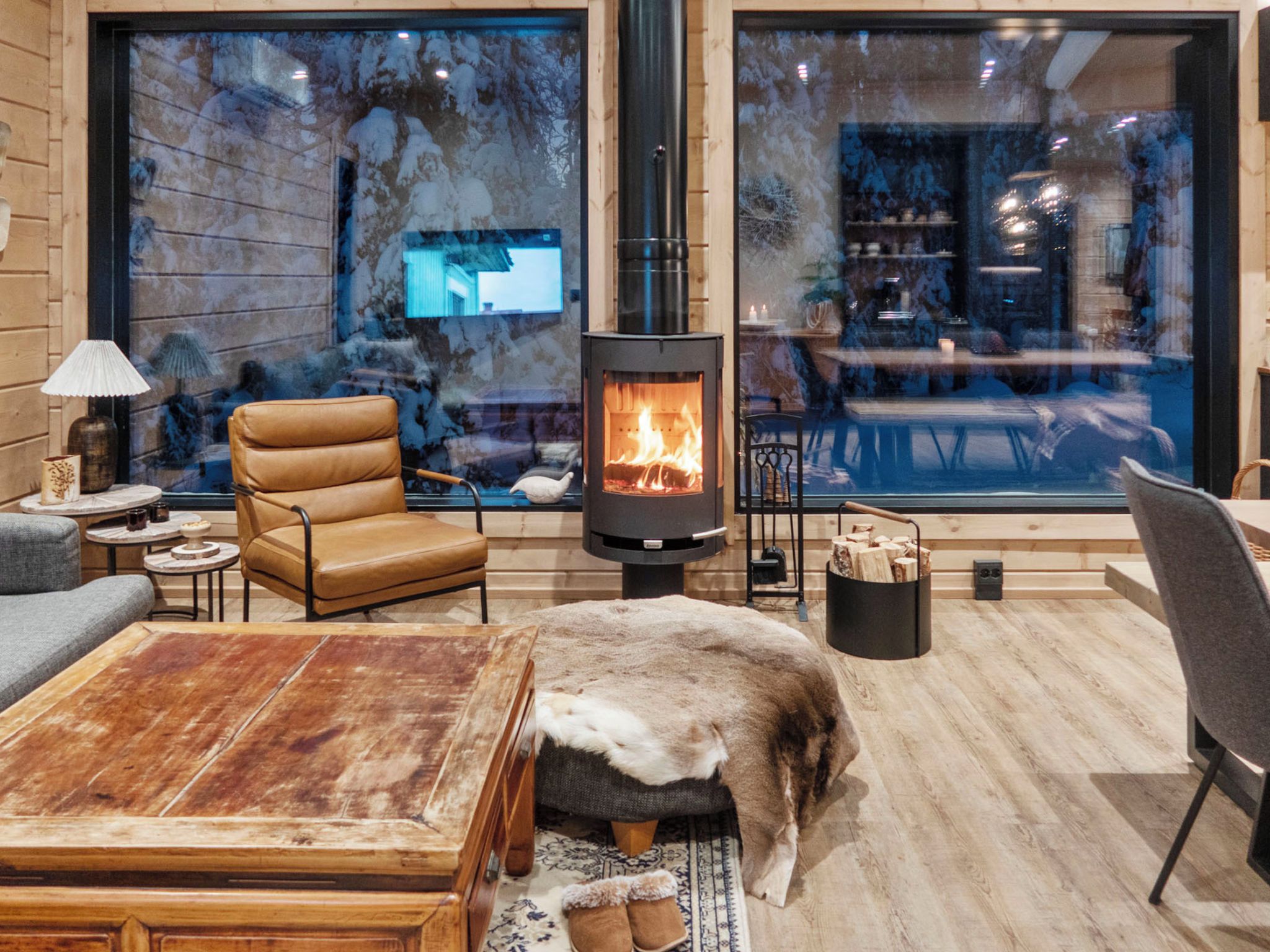 A cozy living room with a large fireplace, leather furniture, and a view of the outdoors through large windows.