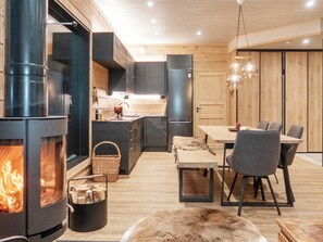 A modern kitchen with a wood-burning stove, a dining area with a table and chairs, and a cozy seating area with a fur throw. - Villa huili by Interhome (Kuusamo)