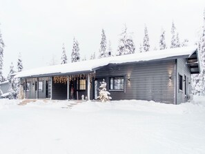 Una cabaña de madera con un porche, rodeada de árboles cubiertos de nieve.