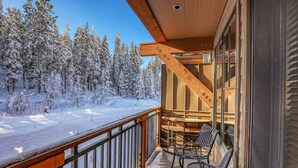 A balcony with wooden railings, a seating area with chairs, and a view of snow-covered trees and a ski slope. - Big Horn Lodge 410 - Platinum Slopeside Residence (Truckee)
