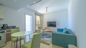 Een moderne woonkamer met een bank, een televisie, een eethoek met stoelen en een keuken met apparatuur.