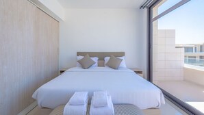 Een moderne hotelkamer met een groot bed, twee kussens, een nachtkastje en uitzicht op de stad door een groot raam.