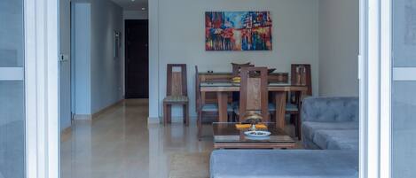 A modern living room with a sofa, a dining table with chairs, a chandelier, and a painting on the wall.