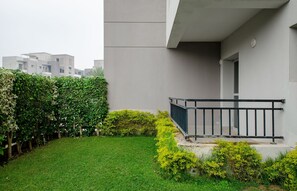 Un edificio moderno con techo plano, un balcón con barandilla negra y un jardín bien cuidado con arbustos.
