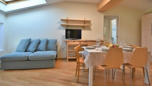 Ein modernes Wohnzimmer mit einer Couch, einem Esstisch für vier Personen, einem Fernseher und einem Oberlicht.