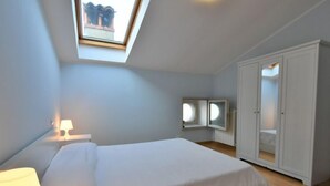 Ein Schlafzimmer mit Oberlicht, einem Bett, einem Kleiderschrank und einem Nachttisch mit Lampe.