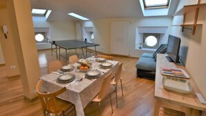 Ein modernes Apartment mit Essbereich, einer Couch, einem Fernseher und Dachfenstern.
