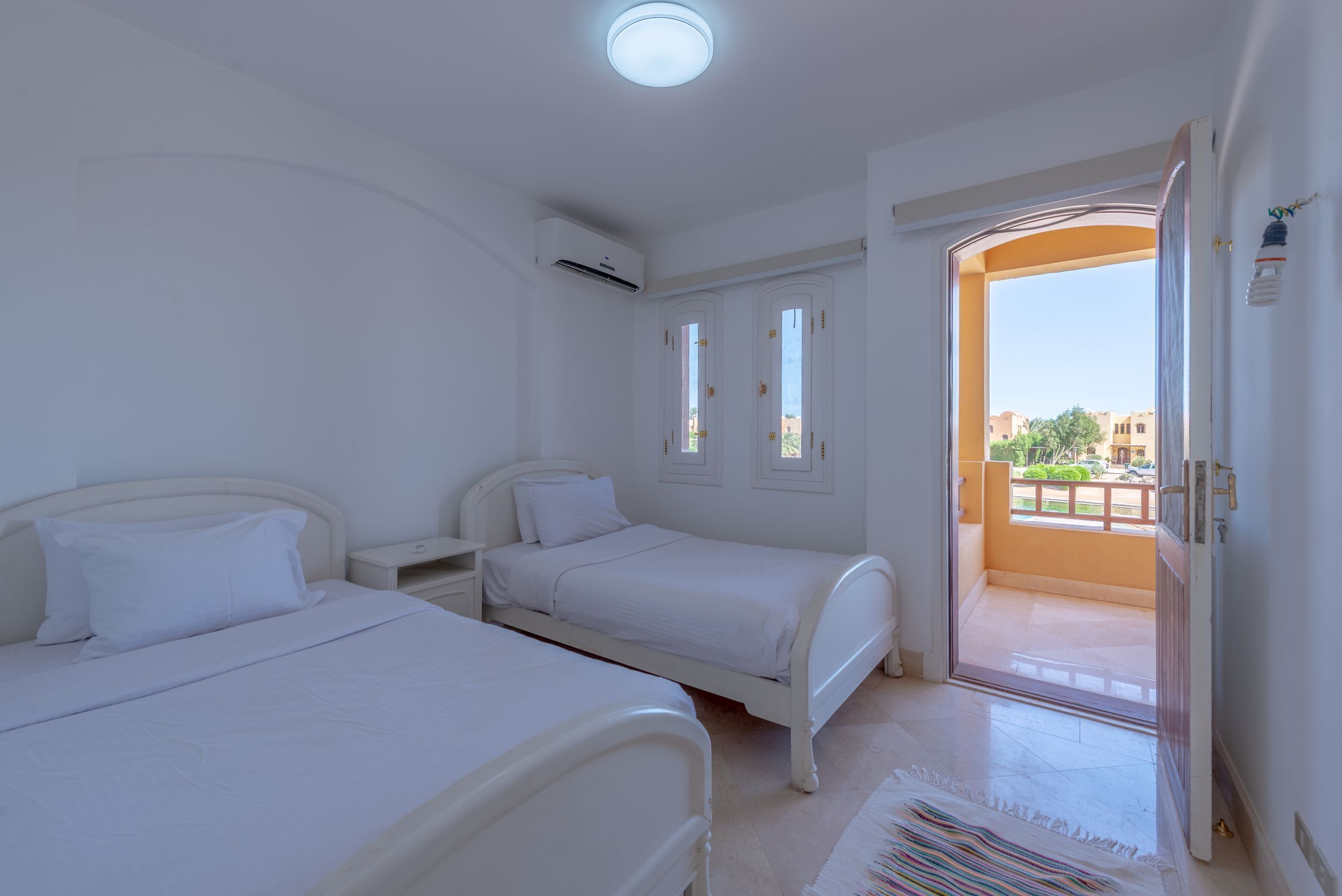 A bedroom with two beds, a nightstand, an air conditioning unit, and a view of the outside balcony.