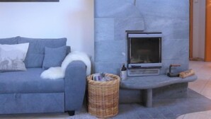 A modern living room with a grey sofa, a fireplace, and a painting of mountains. - Arbgrat by Interhome (Täsch)